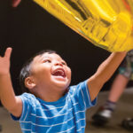 A toddler playing with helium balloons at the Warhol