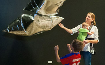 A woman and her two children play with helium balloons at the Warhol Museum